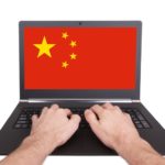 Image of Chinese flag on laptop computer screen; hands typing.