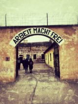 Visitors beneath a sign reading 'arbeit macht frei' (which translates to 'work makes you free') at the small fortress at Terezin concentration camp in Czech Republic. Photo credit: M. Ciavardini.