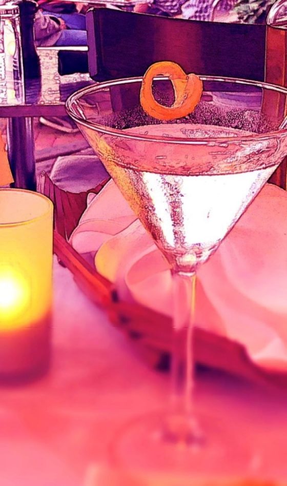 Am image of a martini in a martini glass, a bread basket, and a candle on a restaurant table. Photo credit: L. Tripoli.